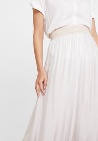 Lange, vloeiende rok van lichtgewicht, doorschijnende stof. Heeft een smock tailleband in een neutrale tint, met een zachte, gestructureerde afwerking. Kleur: gebroken wit.