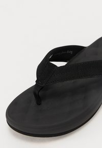 Black flip-flop featuring textured rubber sole and fabric straps with a chevron pattern. Minimalist design with a smooth finish.