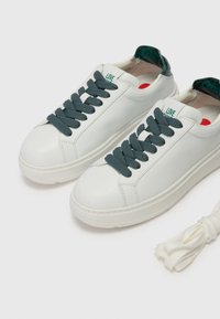 Balti ādas tenisi ar pelēkām auklām un struktūrētu zaļu akcentu uz papēža. Iekļauts papildus balto auklu pāris.