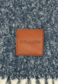 Tissu en laine bleu avec des taches blanches, doté d'un patch en cuir marron embossé avec "COACH" et d'une couture détaillée.