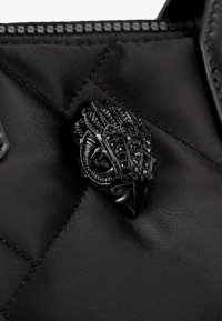 Borsa in nylon trapuntato nera con un prominente spilla nera ornata che presenta accenti lucidi e dettagli intricati che ricordano la testa di un uccello.