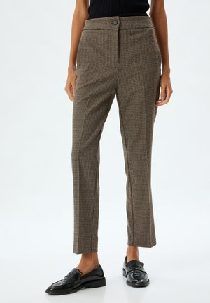 Pantalons en motif pied-de-poule marron avec une coupe droite, taille haute, fermeture à un bouton et pli avant élégant. Associés à des mocassins noirs.