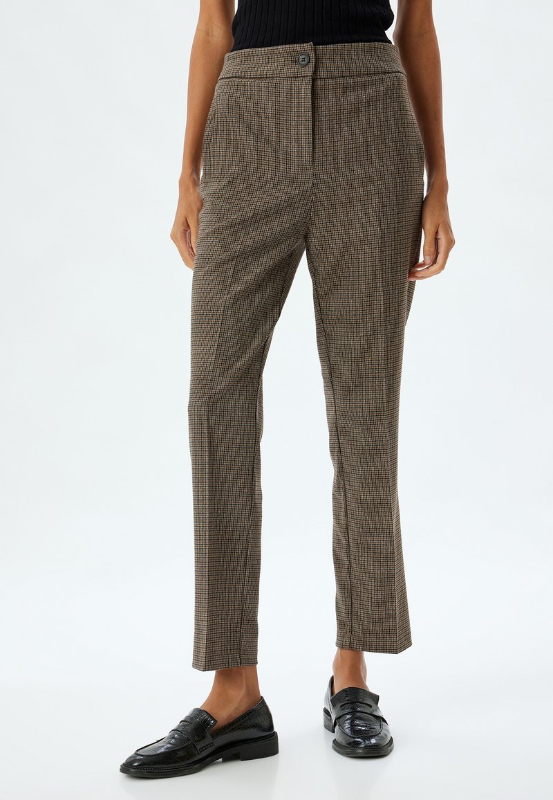 Hosen mit braunem Hahnentrittmuster im geraden Schnitt, hoher Taille, einem Knopfverschluss und einer eleganten Vorderfalte. Dazu passen schwarze Loafers.