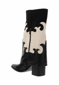 Bota de cuero blanco y negro hasta la mitad de la pantorrilla con patrones decorativos en espiral, cremallera lateral, punta afilada y tacón cuadrado.
