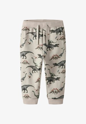 Gyermek bézs színű jogging nadrág elasztikus derékrésszel és dinoszaurusz mintával, amely T-Rexet, stegoszauruszt, brachioszauruszt és pterodaktilt ábrázol.