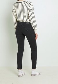 Jeans negros ajustados con una cintura alta y un dobladillo con ligero desgaste. Combinados con un suéter de rayas crema y zapatillas de deporte blancas de caña alta.