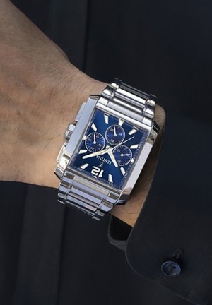 Montre en acier inoxydable argenté avec un cadran rectangulaire bleu, trois sous-cadrans et des index horaires audacieux. Dotée d'un bracelet à maillons.