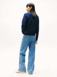 Sweat-shirt navy à manches longues, associé à un jean large bleu clair et des baskets blanches. Texture lisse et coupe décontractée.