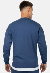 Felpa blu navy con texture a coste, maniche lunghe e scollo rotondo. Presenta un orlo leggermente curvato e dettagli di cucitura.