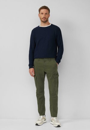 Marineblauer Strukturpullover mit weißem Rundhalsausschnitt, kombiniert mit olivgrünen Cargo-Hosen mit Seitentaschen. Legere Schuhe runden das Outfit ab.