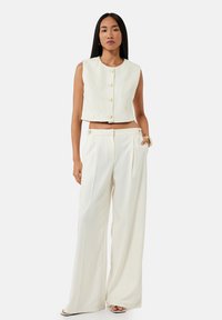 Top corto bianco con texture floreale e bottoni rotondi, abbinato a pantaloni a vita alta e gamba larga dello stesso colore.