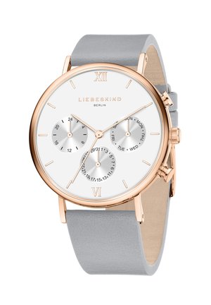 Rund ur med en hvid skive, tre sub-skiver, rosaguld detaljer og et gråt læderrem. Har romertal ved 12 og 6.