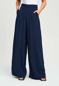 Mornarske široke hlače s plisama, visokim strukom i bočnim džepovima. Izrađene od laganog materijala, s glatkom teksturom i čistim linijama.