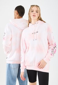 Felpa rosa tie-dye con maniche lunghe, caratterizzata da ricami floreali sulle maniche, tasca a marsupio e cappuccio regolabile con lacci.