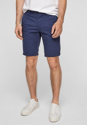 Marineblaue Baumwollshorts mit strukturierter Oberfläche, umgeschlagenem Saum, Seitentaschen und einem Bund mit Gürtelschlaufen, kombiniert mit weißen Sneakers.