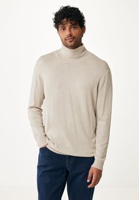 Maglione beige a collo alto con una texture morbida e liscia, abbinato a pantaloni in denim blu scuro. Le maniche sono aderenti con polsini a costine.