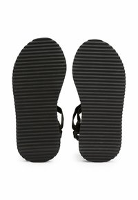 Suelas de sandalias de goma negra con ranuras horizontales para tracción; las correas son visibles pero no prominentes. Forma general plana y ovalada.