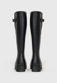Pair of black knee-high rubber boots with buckles on the sides, shown from the back on a white background.