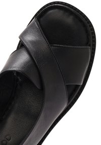 Sandalio in pelle nera con cinturini incrociati, superficie liscia, punta tonda e suola piatta con bordo testurizzato.