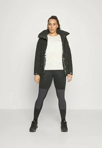 Crna jakna preko bijele košulje, uparena s crnim i sivim tajicama. Atletska obuća. Jednostavan dizajn s detaljima gumba i zatvarača.