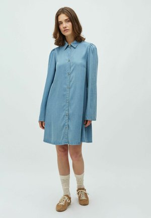 Rochie cămașă din denim albastru deschis, cu mâneci lungi, închidere cu nasturi pe față și guler de cămașă. Purtați cu șosete tricotate crem și pantofi maro.