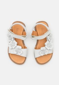 Valkoiset taaperokenkä sandaalit, joissa on vaaleanruskeat sisäpohjat, nilkkastrapit ja koristeelliset valkoiset ja harmaat kukka-applikaatiot etustrappeissa.