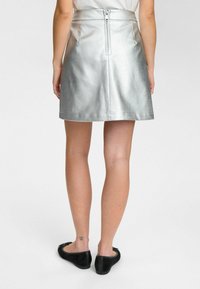 Silver metallic mini kjol med en slät yta, sidodragkedjestängning och en utsvängd silhuett. Kombinerad med svarta platta skor.