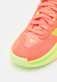 Chaussure de sport rose corail avec semelle, lacets et logo jaune néon, composée de tissu en maille et de surpiqûres synthétiques sur l'avant et le côté supérieur.