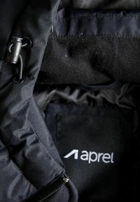 Sort polstret jakke med en glat overflade, lynlåslukning og et mærke med brandnavnet "aprel." Fremtrædende tekstureret stof.