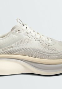 Chaussure de sport beige clair avec dessus en tissu tricoté, fermeture lacets et semelle épaisse rembourrée avec un design en couches.