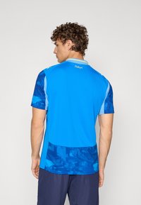 Maglietta sportiva blu con design a gradiente, maniche corte e colletto. La texture è liscia con una sezione inferiore decorata.