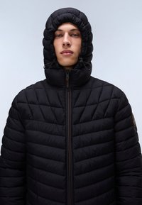 Black quilted puffer jacket with a high neck and hood, featuring a front zipper, elastic drawstring, and subtle logo patch on the shoulder.