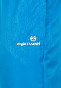 Blauer texturierter Stoff mit glänzender Oberfläche. Merkmale ein weißes Logo mit dem Text "Sergio Tacchini", das auffällig platziert ist.