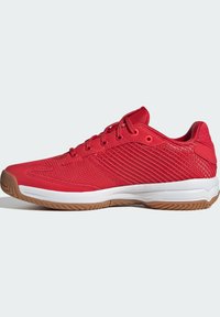 Baskets de sport rouges dotées d'une tige en mesh, de panneaux latéraux texturés, de six œillets et d'une semelle en caoutchouc marron. La semelle intermédiaire blanche met en valeur le design.