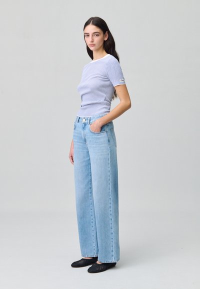 Jeans a vita alta di un blu chiaro con gambe larghe, abbinati a un top aderente a righe blu e bianche a maniche corte. Scarpe nere a slip-on intrecciate.