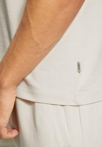 Licht beige overhemden met korte mouwen, een gladde textuur, zijnaad details en een klein stoffen label aan de linksonderzijde.