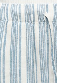 Κοντινό πλάνο λευκού υφάσματος με κάθετες μπλε ρίγες και λεπτομέρεια ελαστικής ζώνης στη μέση.