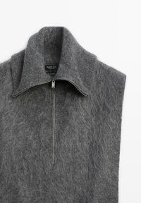 Gilet grigio in cashmere con colletto alto e corta zip. Texture morbida, design minimale e senza maniche, caratterizzato da un aspetto delicato e peloso.