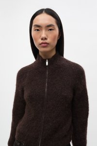 Pulover maro, pufos, cu fermoar și guler înalt, realizat din material moale, cu un fermoar argintiu și o siluetă ajustată.