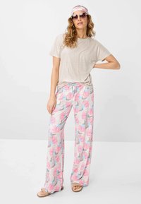 T-shirt loose color beige chiaro, pantaloni a palazzo con pattern floreale rosa, grigio e blu, abbinati a un cerchietto e occhiali da sole oversize.