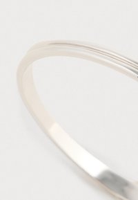 Bracciale a cerchio in argento semplice con superficie liscia e lucida e bordi arrotondati. Presenta un leggero design a spirale e nessuna decorazione visibile.