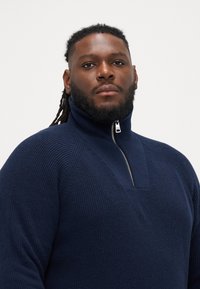 Σαλοπέτα πουλόβερ με φερμουάρ σε ναυτικό μπλε, με υψηλό γιακά, κατασκευασμένη από υλικό υφασμάτινης πλέξης και με σχέδιο σε σχήμα V στην περιοχή του λαιμού.