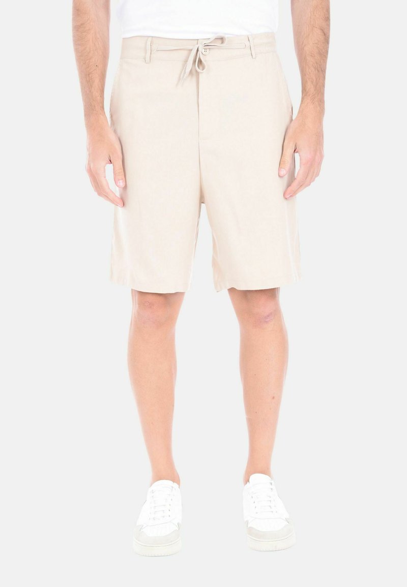Pantaloni corti beige, lunghi fino al ginocchio, realizzati in tessuto leggero, con vita regolabile e due tasche laterali. Indossati con sneakers bianche.
