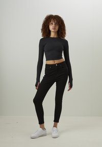Top cropped preto de manga longa emparelhado com jeans ajustados pretos e ténis brancos; tecido suave, design ajustado e estilo minimalista.
