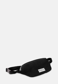 Black fabric fanny pack with a zippered closure, flat design, adjustable strap, and a small white logo label on the front.