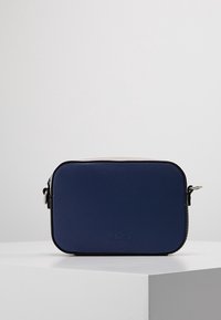 Modrá obdélníková taška vyrobená z texturovaného materiálu, s uzávěrem na zip a nastavitelným popruhem. Mírně zaoblené hrany s detailem loga.