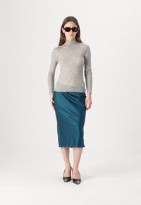 Lys grå, ribbet høyhalset genser kombinert med en teal sateng midi-skjørt. Modellen har på seg svarte, kantede solbriller og blanke svarte hæler.