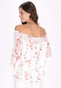 Off-the-shoulder hvid bluse med pink blomsterprint, smocket halsudskæring, lange gennemsigtige ærmer med flæser ved manchetten og en afslappet pasform.