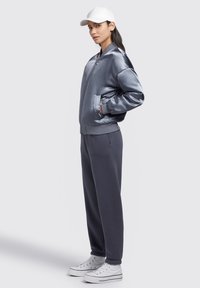 Jachetă bomber din satin de culoare gri deschis, cu buzunare laterale, asortată cu pantaloni de trening gri închis și adidași albi cu glezna înaltă, având o șapcă albă.