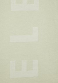 Hellesgrünes, strukturiertes Gewebe mit großen weißen Blockbuchstaben in einer modernen Schriftart, vertikal angeordnet. Minimalistisches Design ohne zusätzliche Muster.